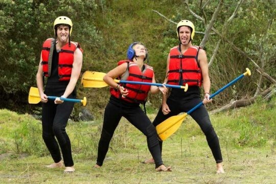 three people holding paddles and wearing lifejackets being funny