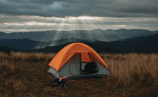 A tent lit up by sun rays in front of the mountains