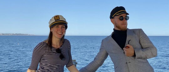 Male and female Checkfront employees wearing captain's hats on a boat