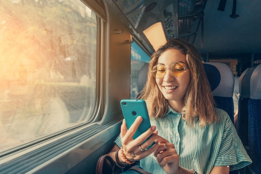 Happy Asian girl checking out booking email on smartphone while riding a train