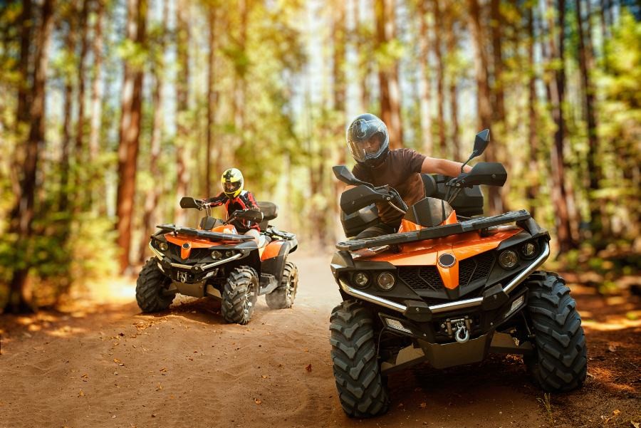 two riders on ATVS driving on a dirt road in a forest