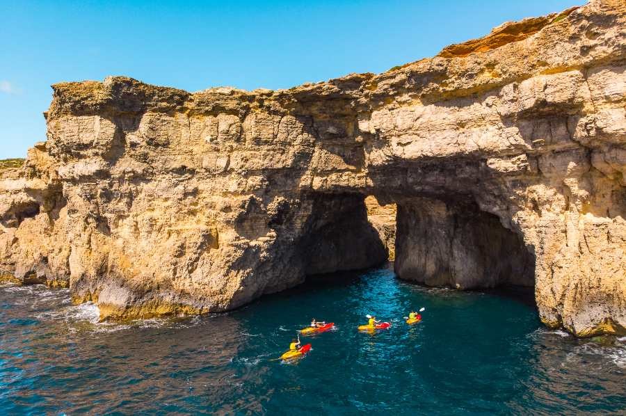 rental business with group of kayakers exploring rock cave in turquoise waters