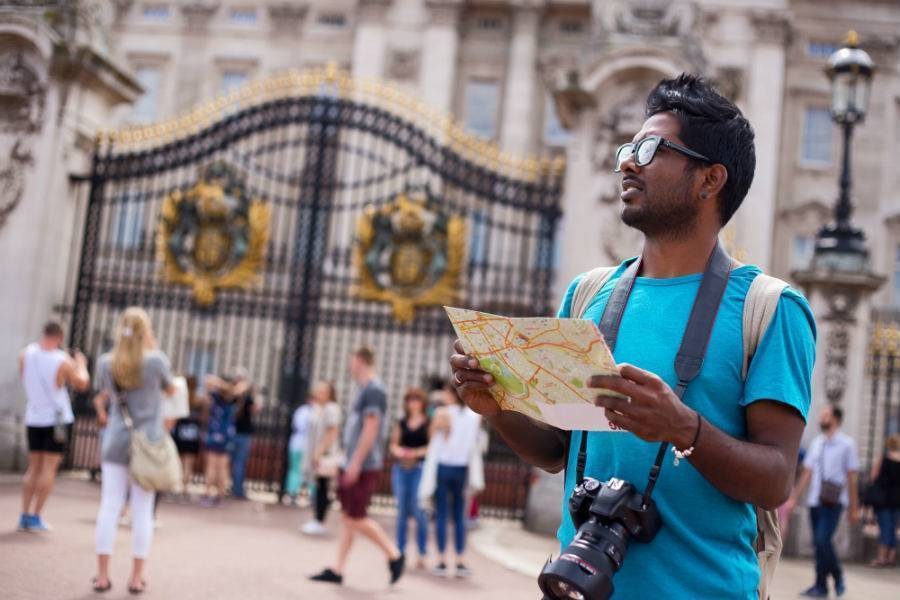 Male traveler reading map with a camera around the neck at Buckingham Palace