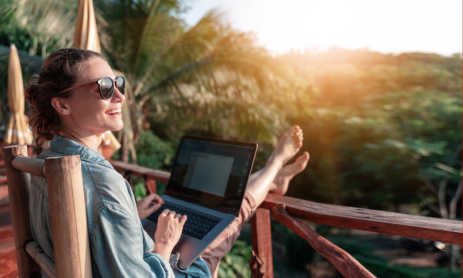 smiling woman sitting on a deck with a laptop looking out into the sun