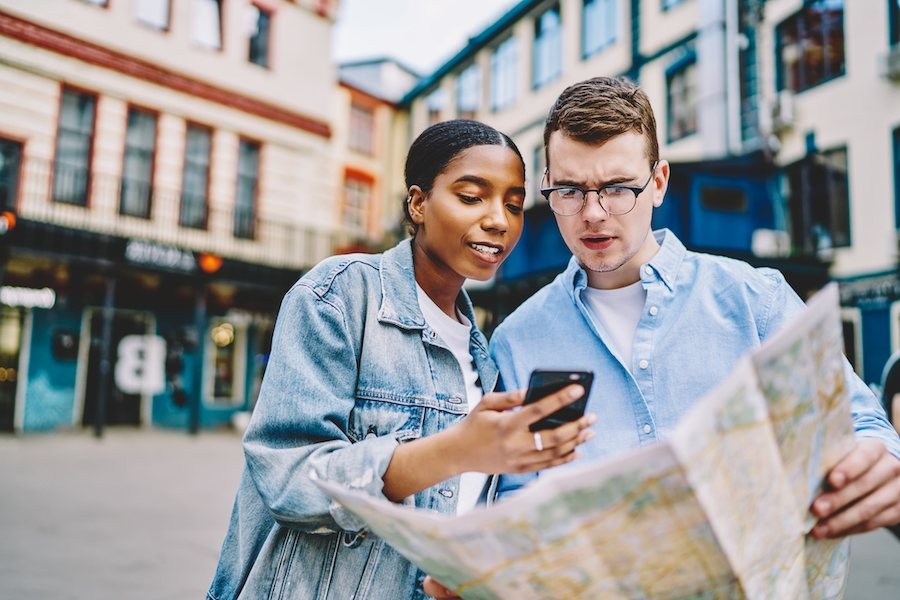 young couple looking at mobile phone while holding map