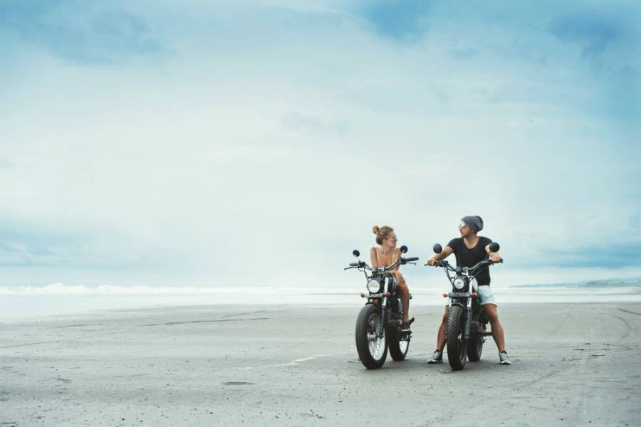 A couple of travelers looking at each other while sitting on motorbikes on the beach