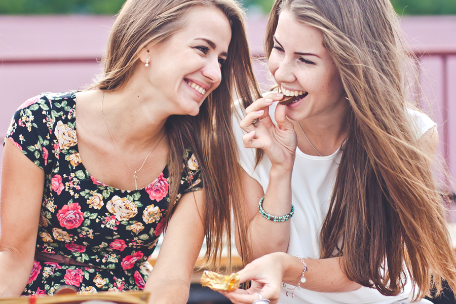 Two female best friends laughing and sharing a piece of chocolate