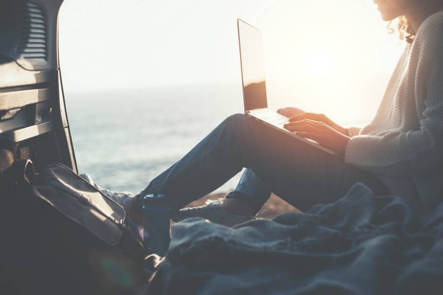 Female traveler working on laptop sitting in van looking at sunset view over ocean