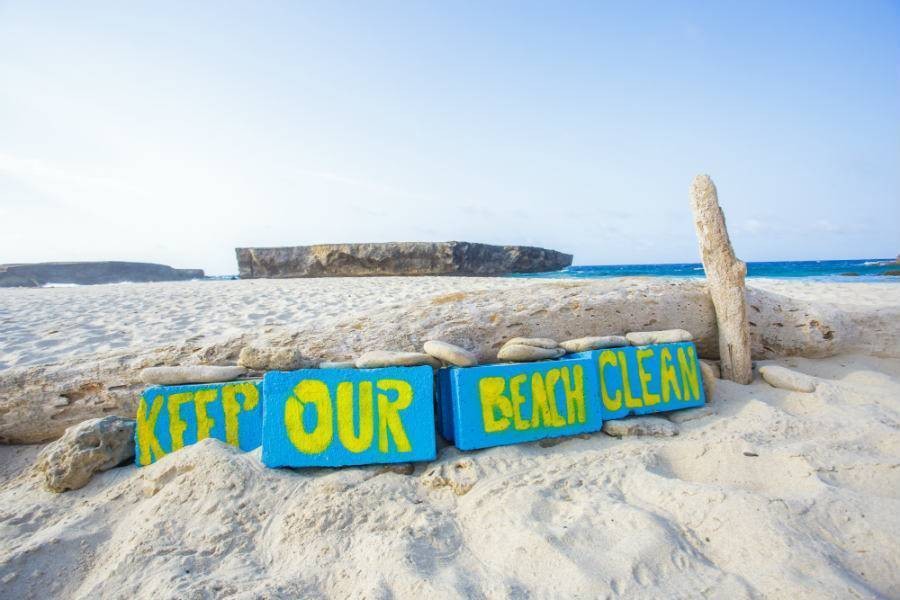 Blue wooden sign on beach with yellow writing saying Keep Our Beach Clean