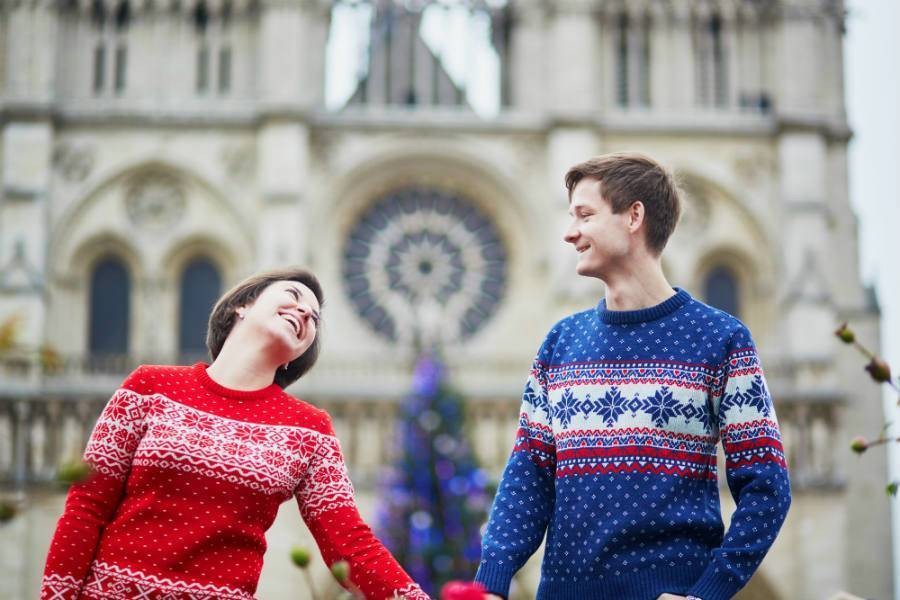 A couple wearing holiday sweaters holding hands in front of Notre Dame at Christmas time