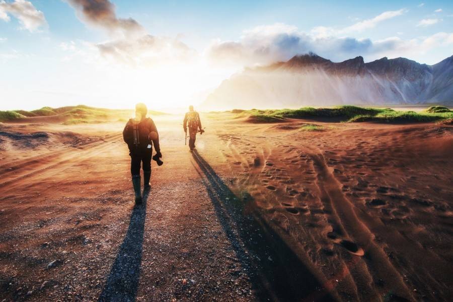 Two male hikers walking on dirt road towards the mountains while the sun is rising