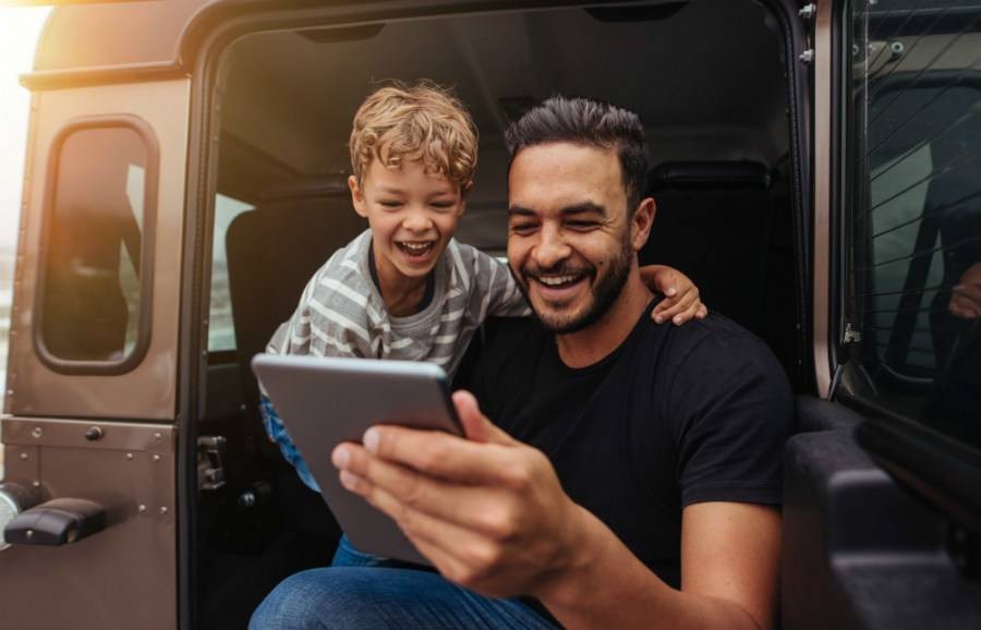 Father and son looking at tablet from car door and laughing.