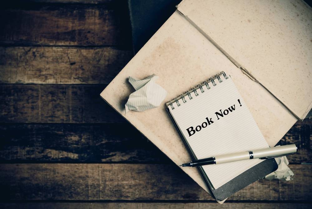 A notebook with "Book Now" written in it