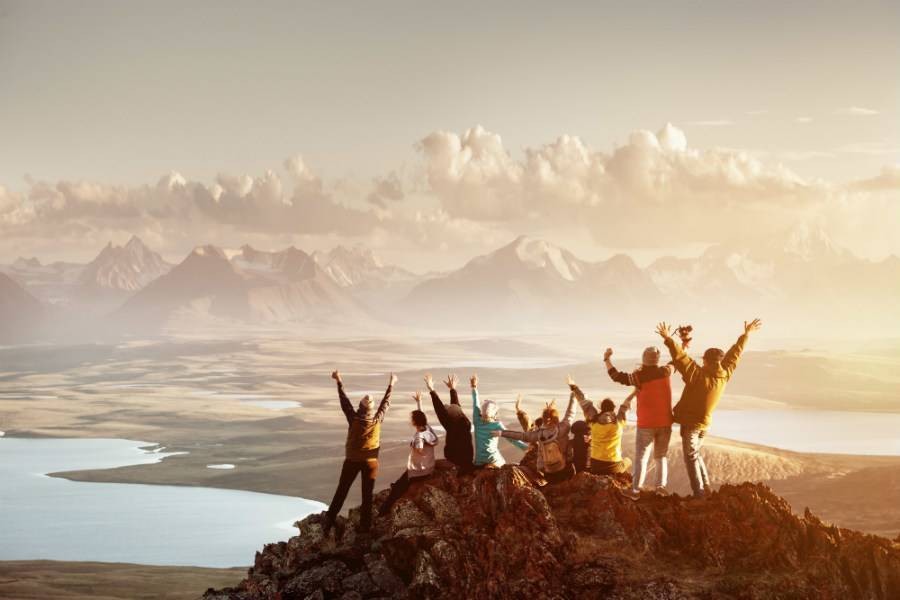 Group of people standing on mountain peak with arms in the air