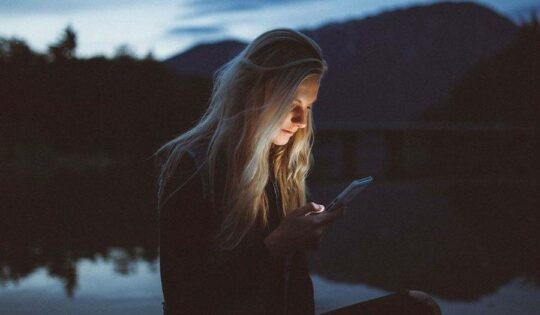 Girl looking at her phone by a lake at night