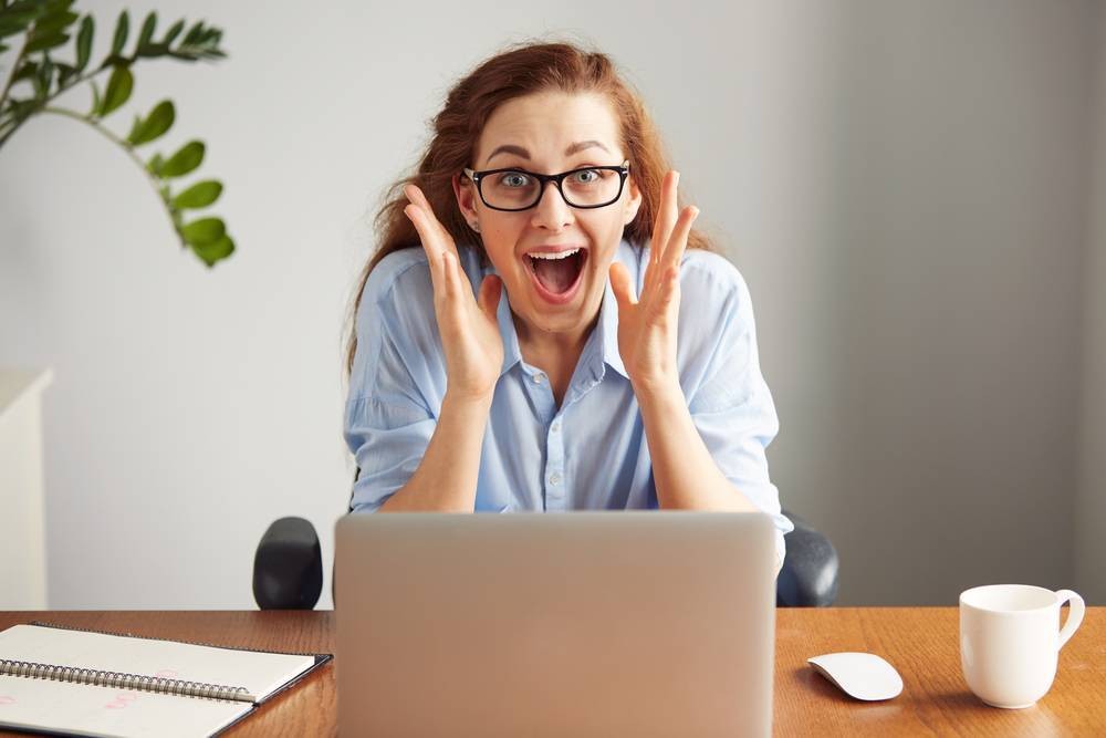 Woman sitting in front of a laptop with a surprised facial expression