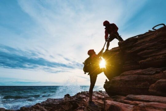 Climbers helping each other on ocean-side cliffs
