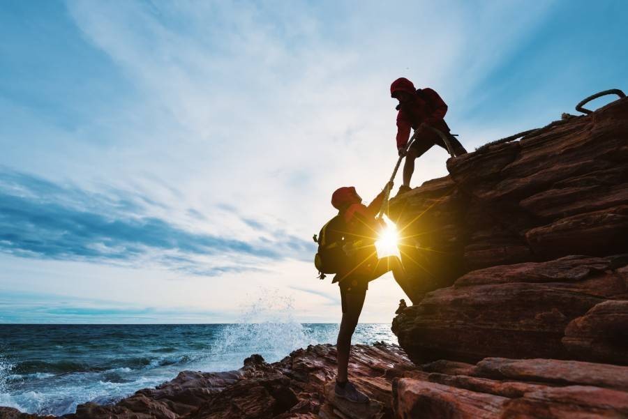 Climbers helping each other on ocean-side cliffs
