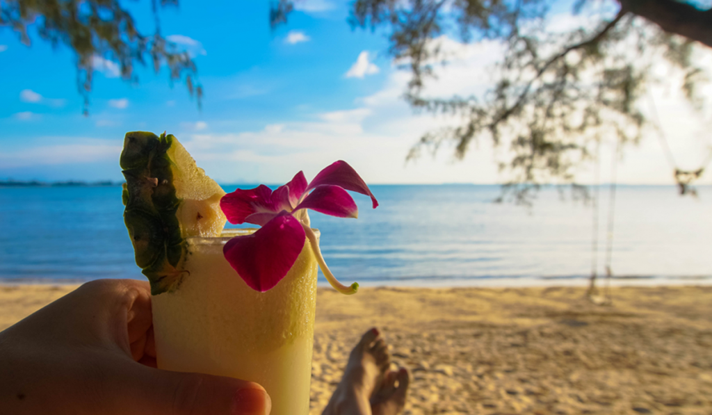 Hand holding a tropical drink on a beach