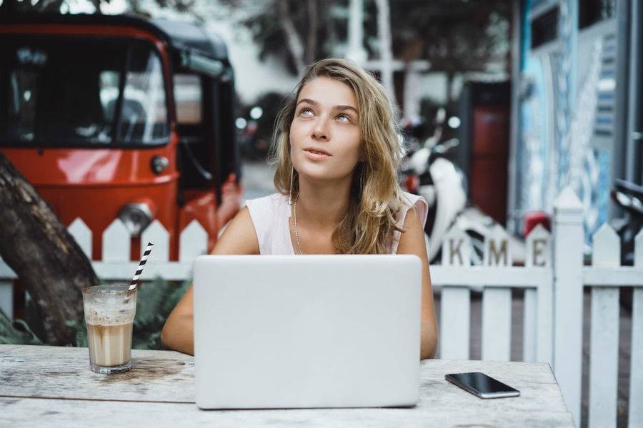Woman sitting in front of laptop, looking up thoughtfully