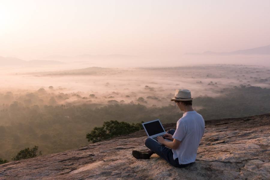 Using a laptop while sitting on a mountain ledge