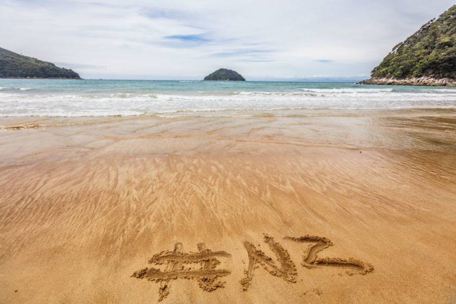 Instagram hashtag #NZ written in the sand with view of ocean