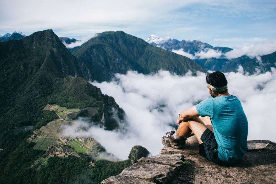 Male traveler on top of mountain over looking cloudy Machu Picchu