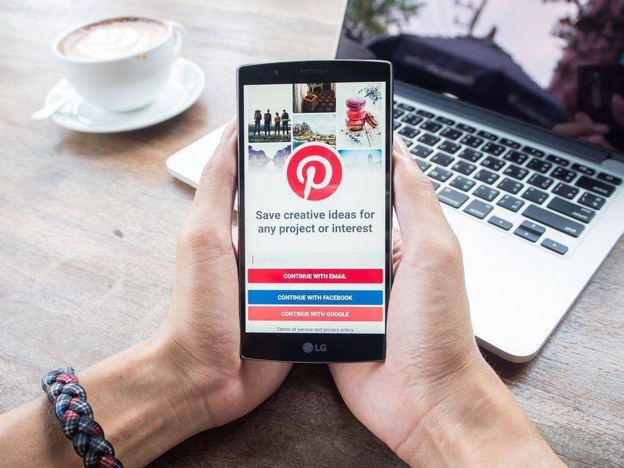 Traveler with Pinterest app open on phone sitting with laptop and coffee