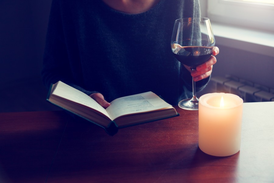 Person reading a booking and holding a glass of wine