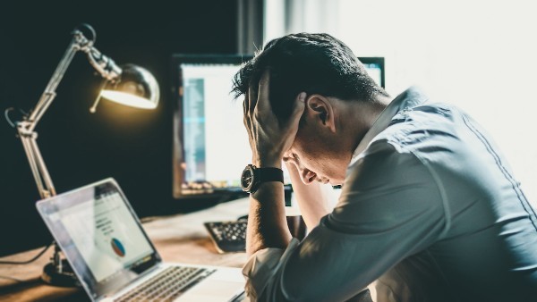 Frustrated man sitting at desk with laptop and holding his head in despair 