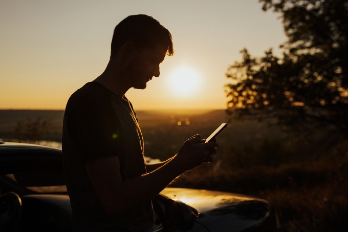 Man sitting outside with sunset behind him reading reviews on phone