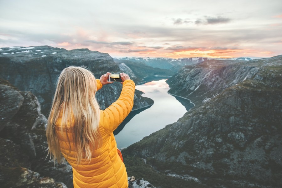 Young blonde woman taking photo of sunset in the mountains