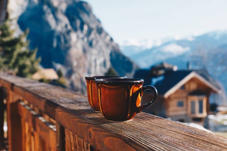 Two hot cocoa mugs on lodge balcony in winter mountain village