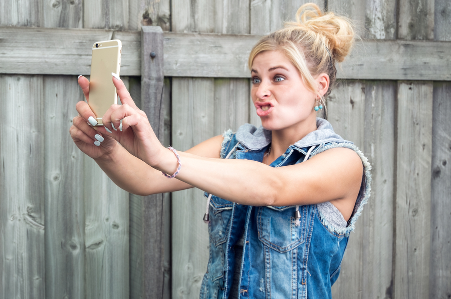 Girl wearing jean jacket vest taking a selfie in front of wooden fence
