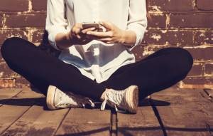 Female sitting on ground with legs crossed looking at phone and head cropped out