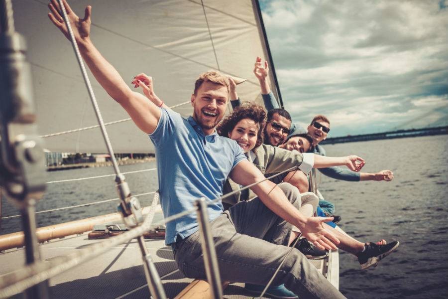 Group of travelers sitting on the edge of on sailboat with arms out wide in celebration