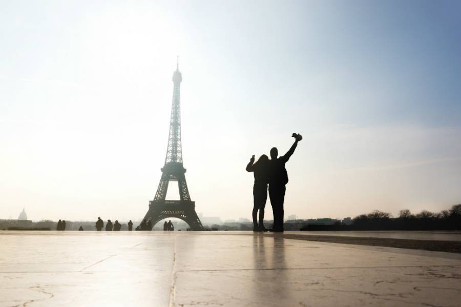 Two travelers looking at the Eiffel Tour at sunset with hands in the air