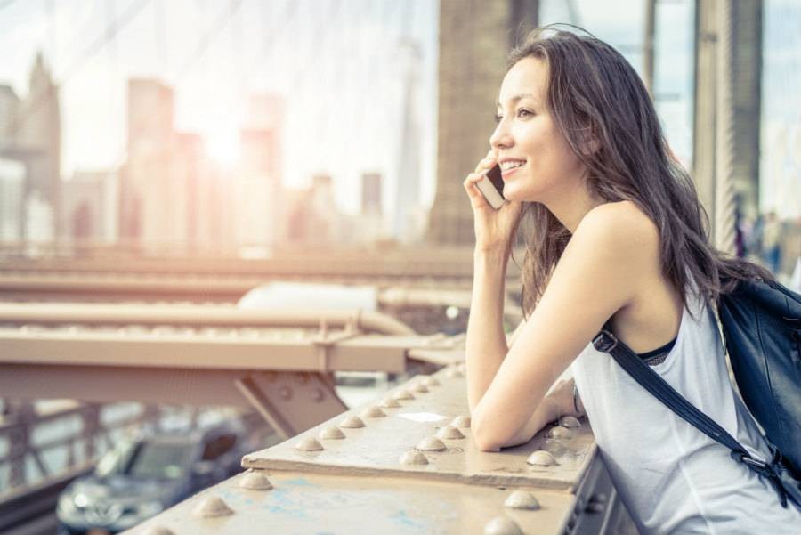 Female traveler leaning on Brooklyn Bridge making a phone booking