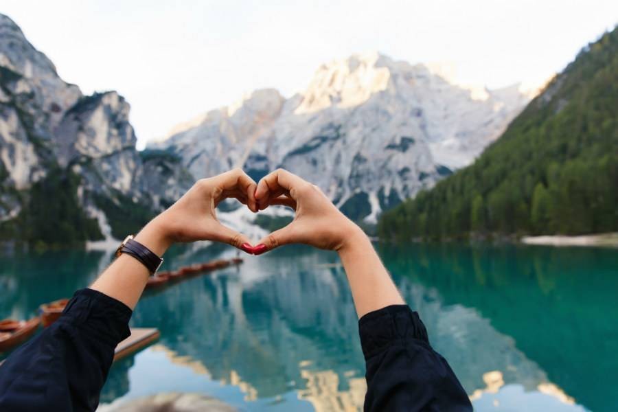 Heart hand signal in front of lake and mountain