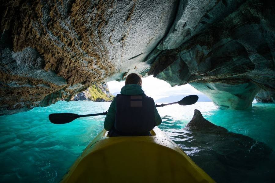 Woman kayaking through cave with turquoise water and interesting patterns on rocks, looking at the opening