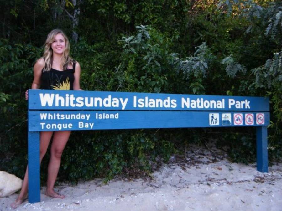 Female solo traveler standing behind Whitsunday Islands National Park sign