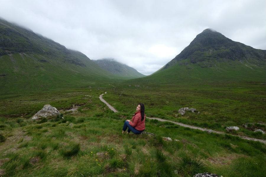 Solo traveler in red jacket sitting down and enjoy view of Scotland Highlands