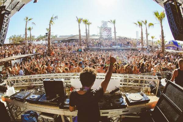 DJ performing to large crowd next to beach