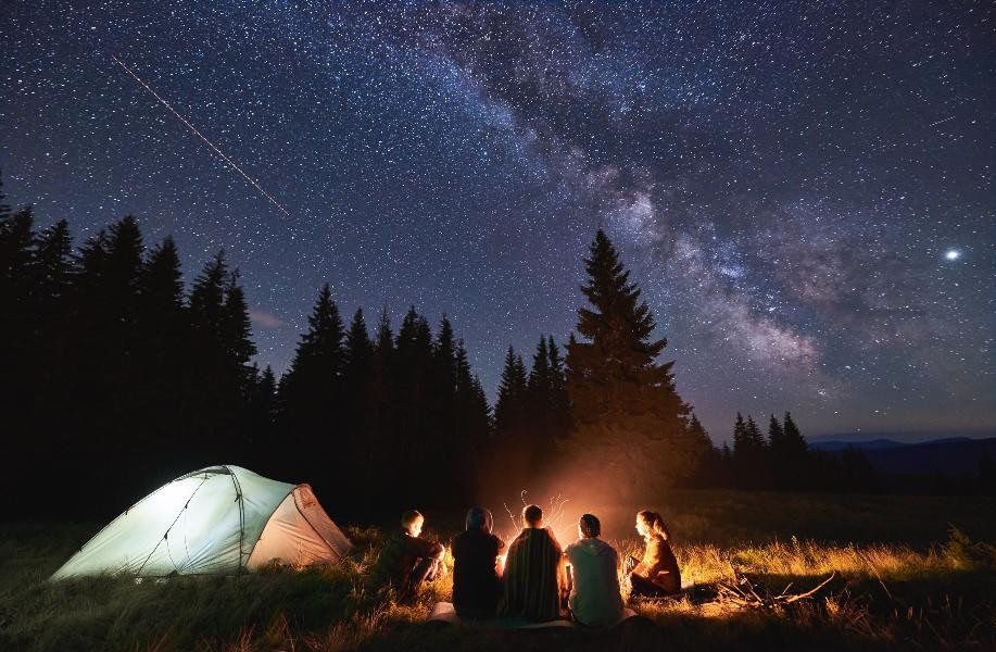 group of friends surround campfire under starry skies