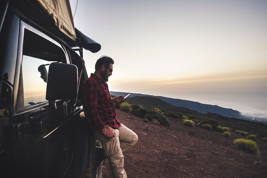 A person leans against their camper while looking at their phone