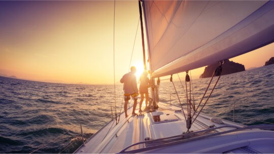 Man and woman standing at the bow of a sailboat at sunset