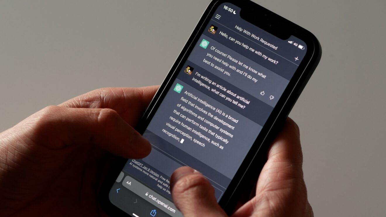 A photo of a person's hands holding a mobile phone. On the phone screen is a chat with ChatGPT asking the AI tool to help the user write a blog about artificial intelligence.
