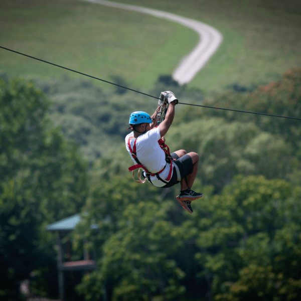 Image of a man in a white shirt, dark shorts and a blue helmet doing a zipline tour at The Wilds. 