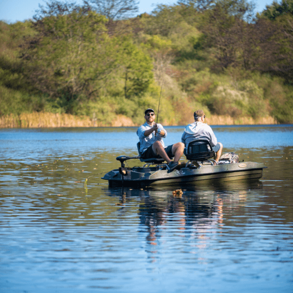 Image of two men doing a fishing tour at The Wilds. They are in a small boat fishing together on a calm lake surrounding by green trees and long grass
